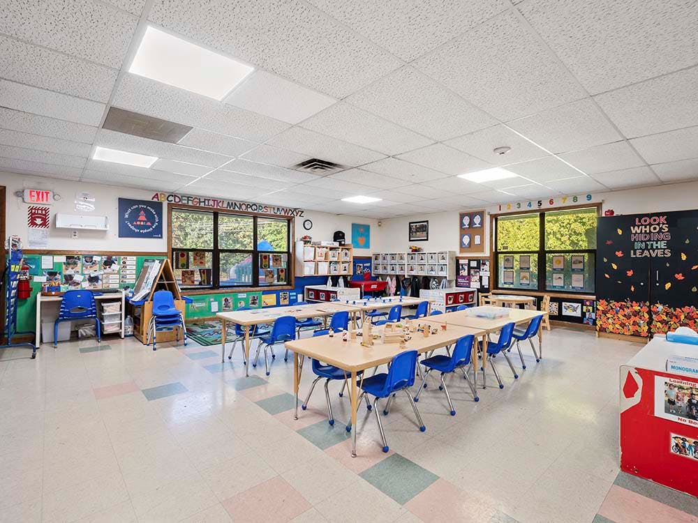 Classroom with small tables and chairs, and windows overlooking trees