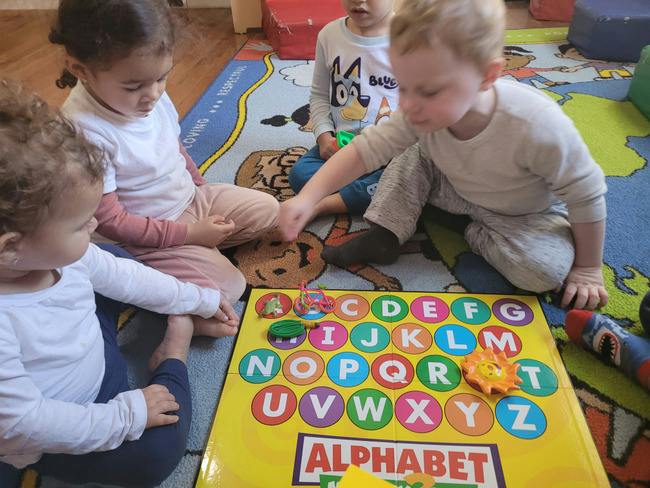 Children sitting on a rug playing with an alphabet learning board