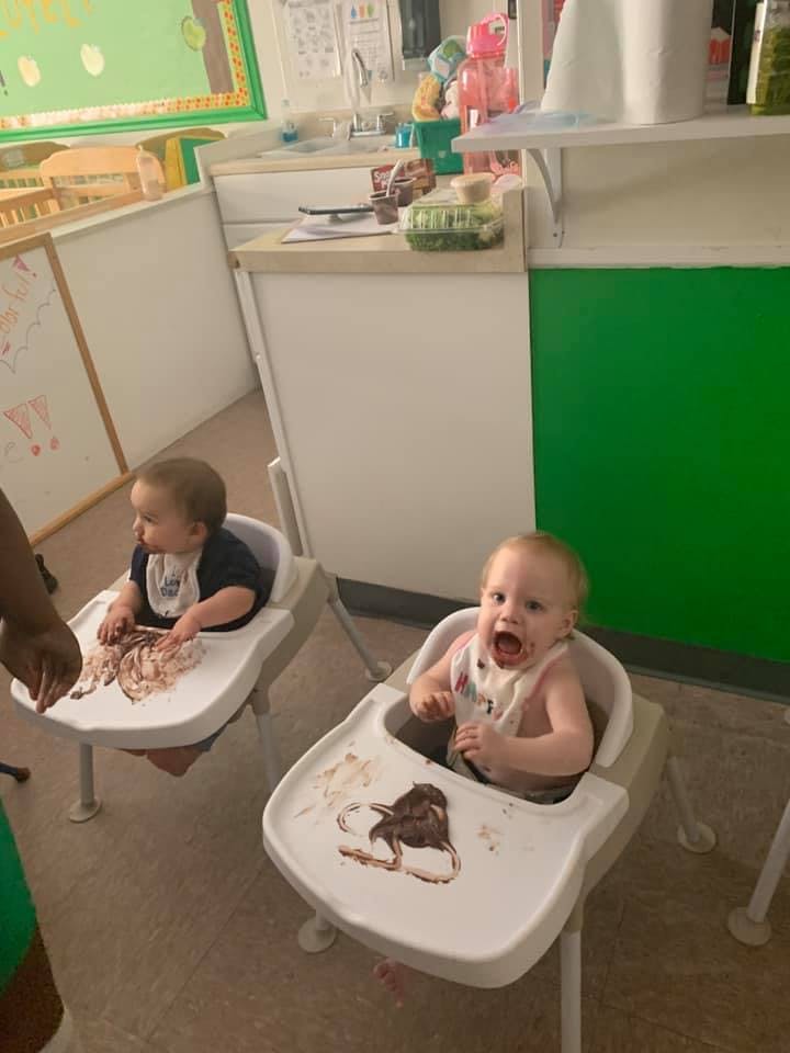 Two children in high chairs with food on their trays