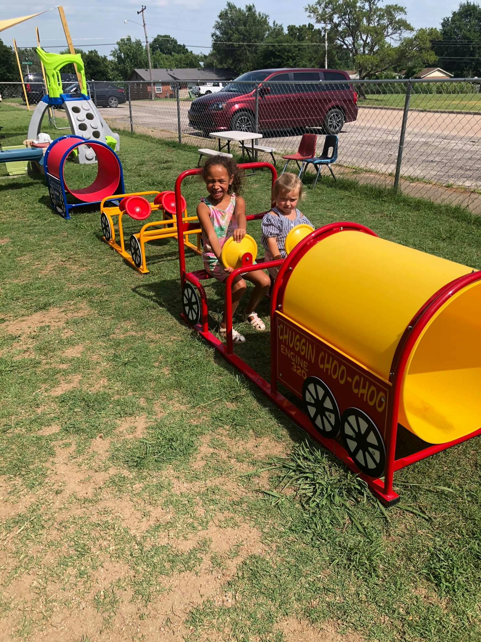 Two children playing on a toy train on a grassy area