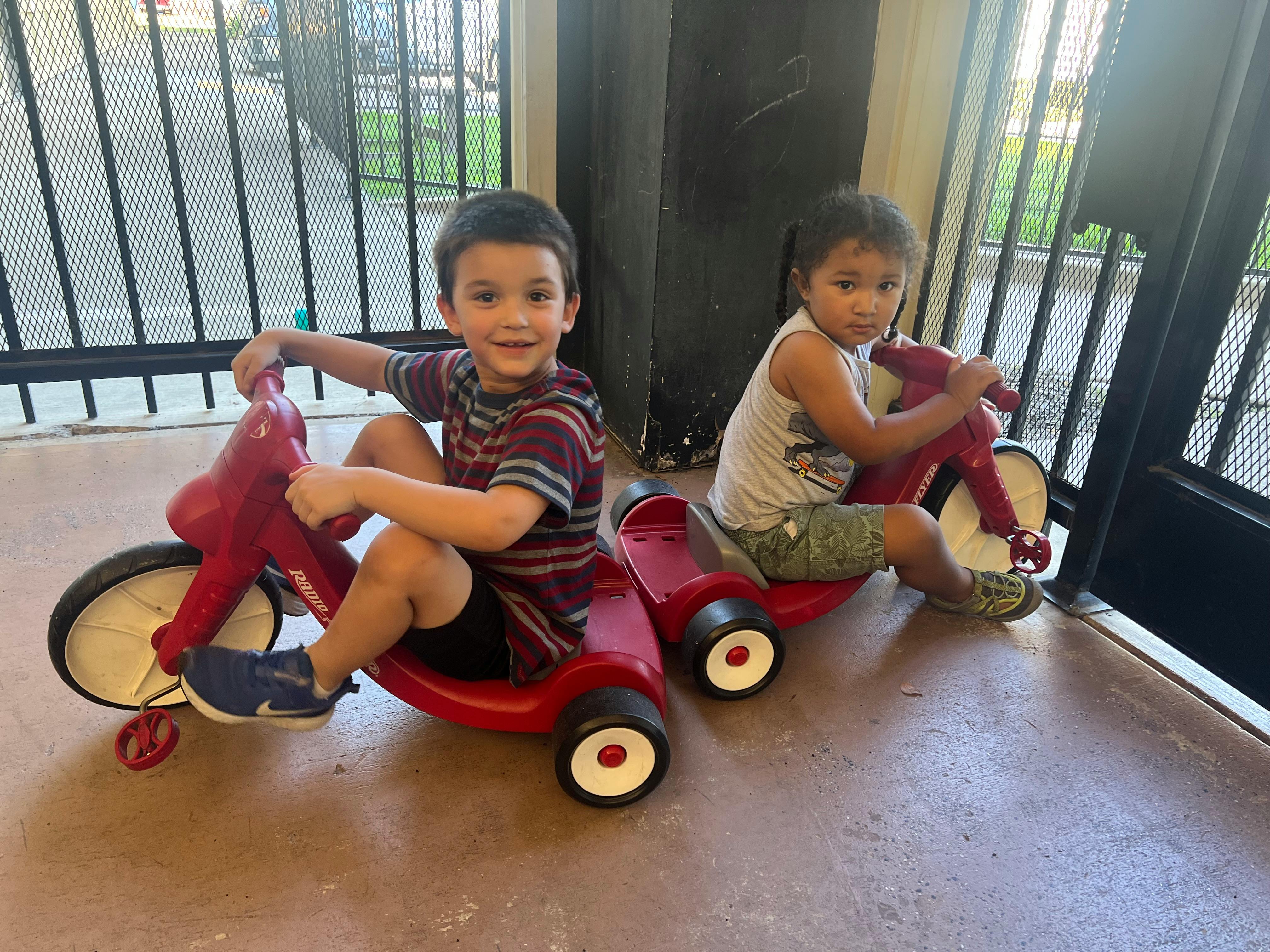 Two children sitting on red tricycles
