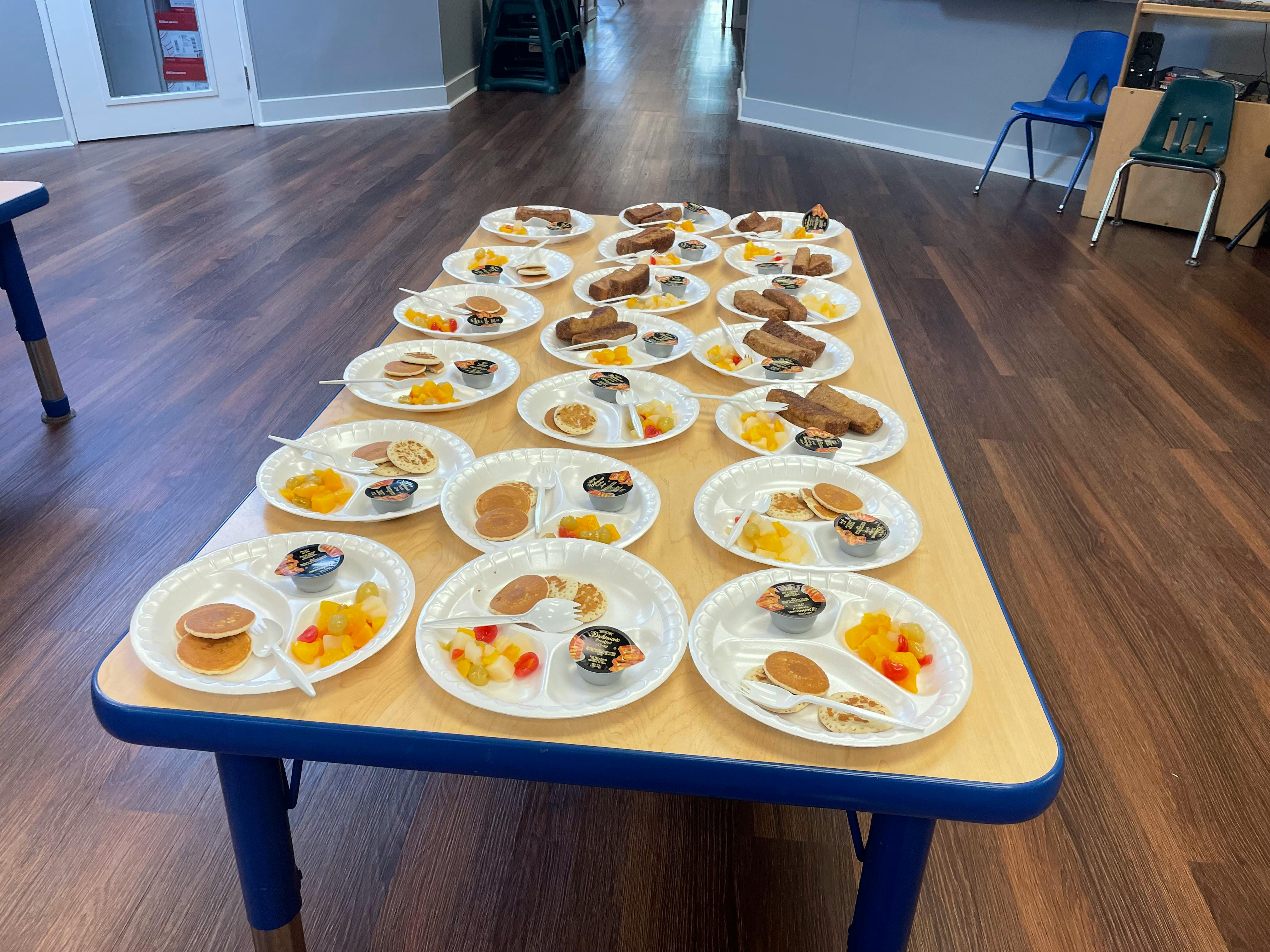 Table with multiple plates of food, pancakes, fruit, and other food items