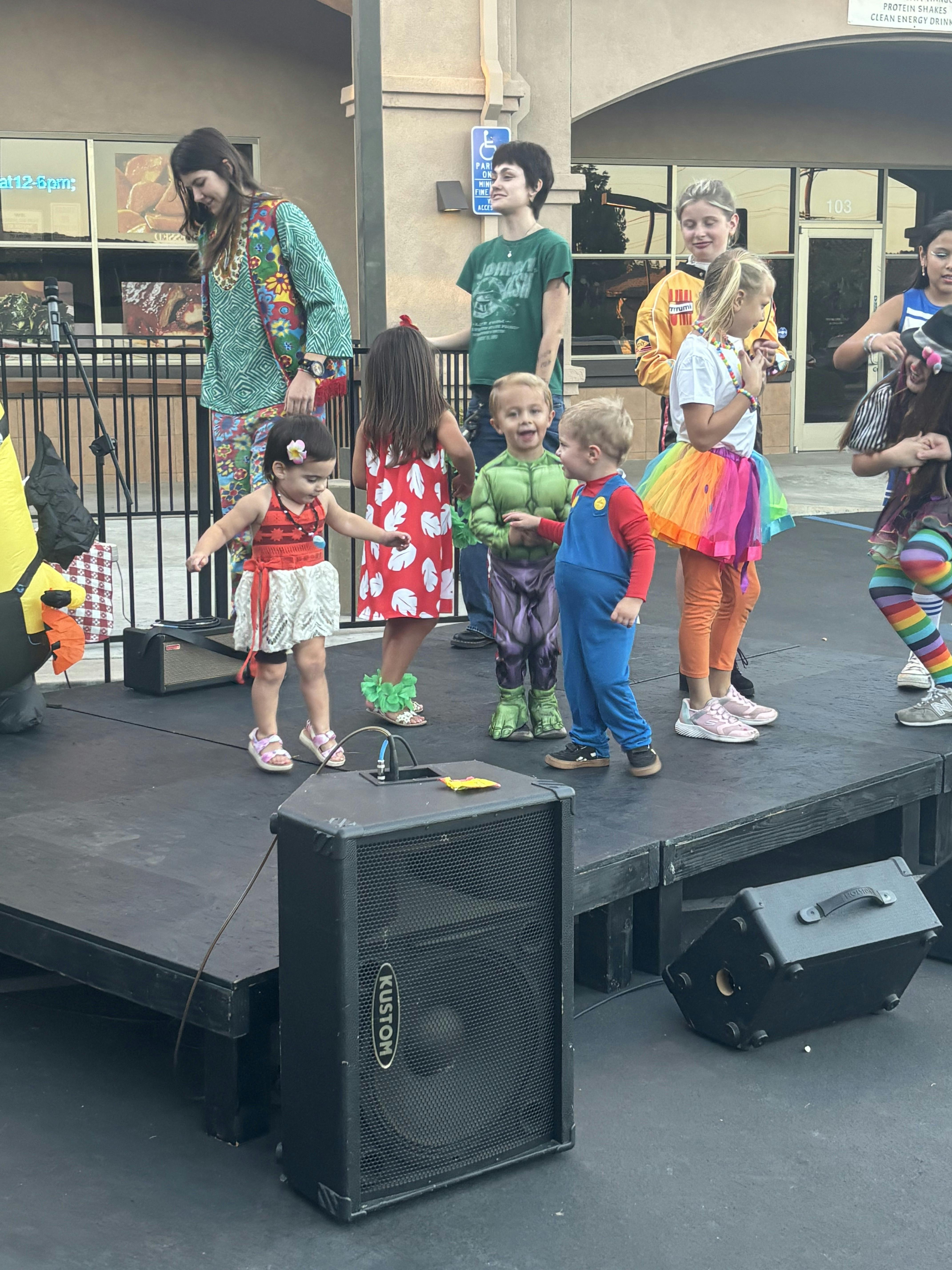Group of children in various costumes standing on a stage at an outdoor event