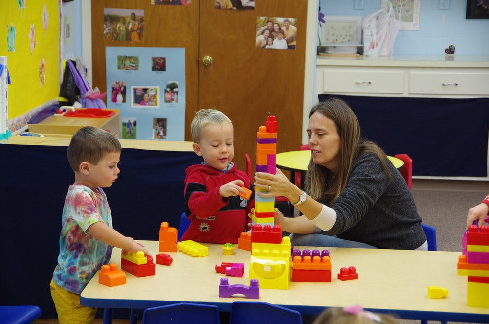 Two children and an adult building with colorful blocks at a table