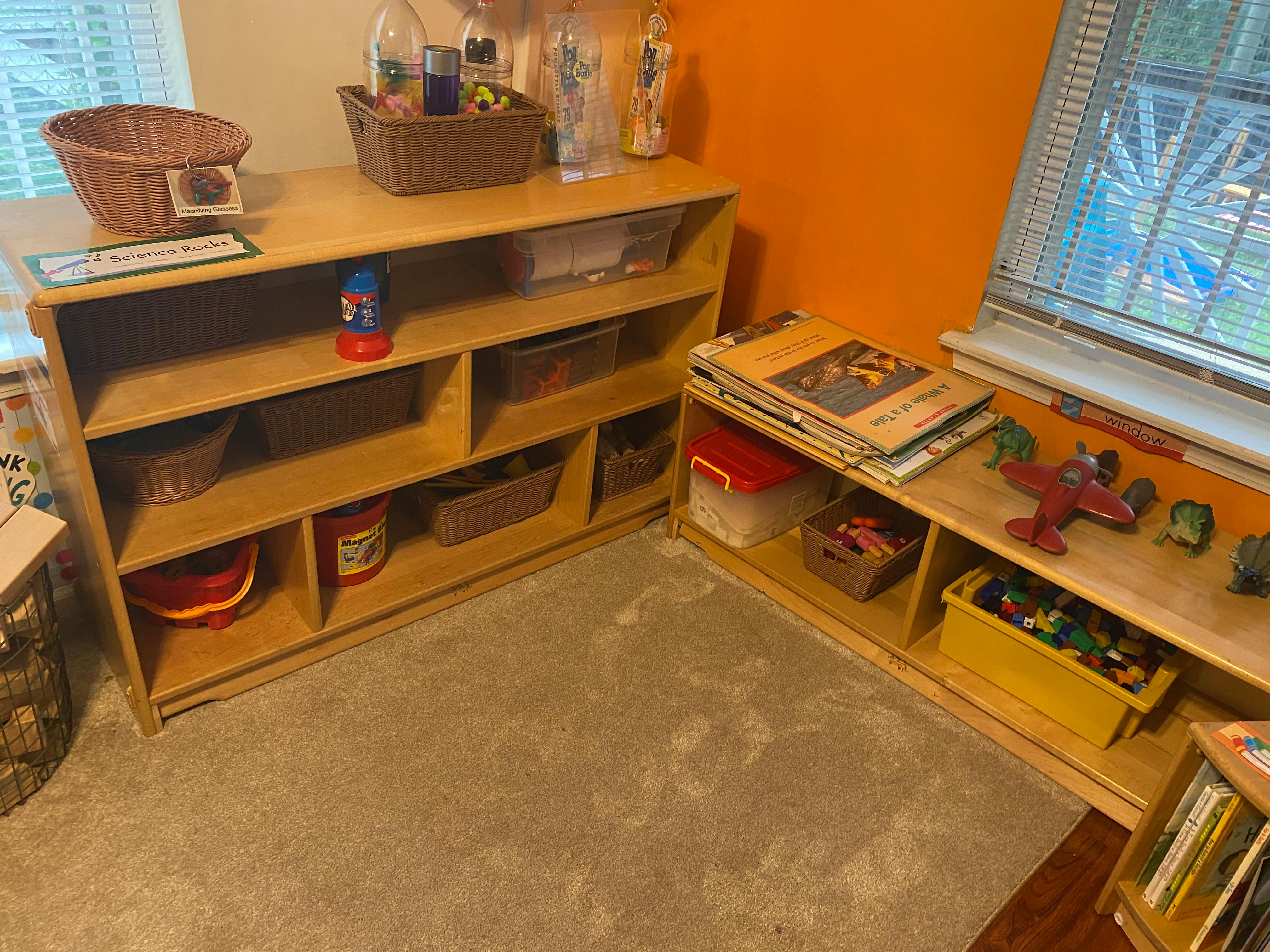 Two wooden shelving units with various items and toys in a room with orange walls