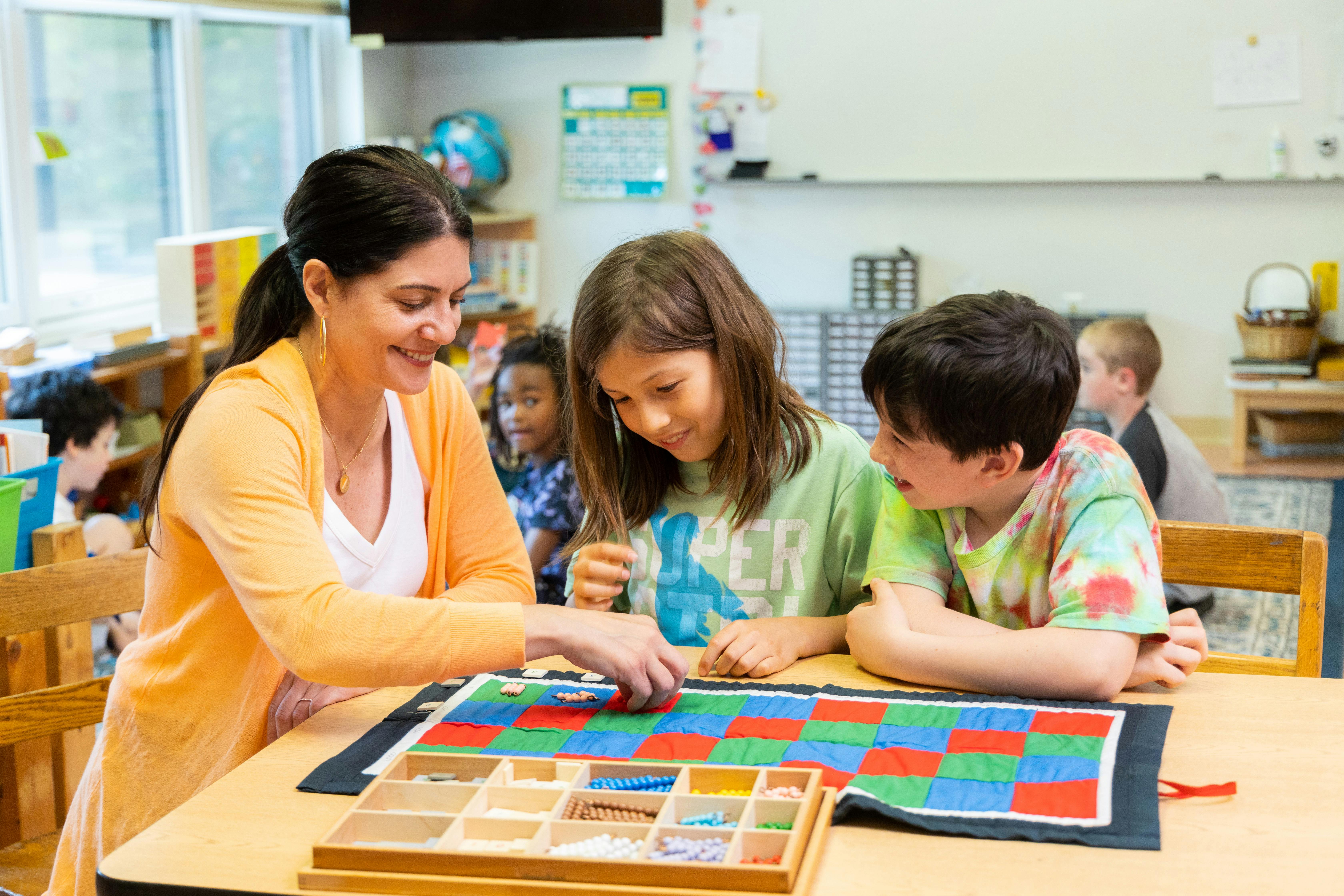Person and two children playing a board game in a classroom