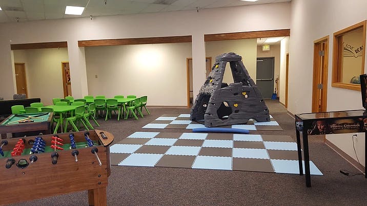 Indoor play area with foosball table, green tables and chairs, and climbing structure