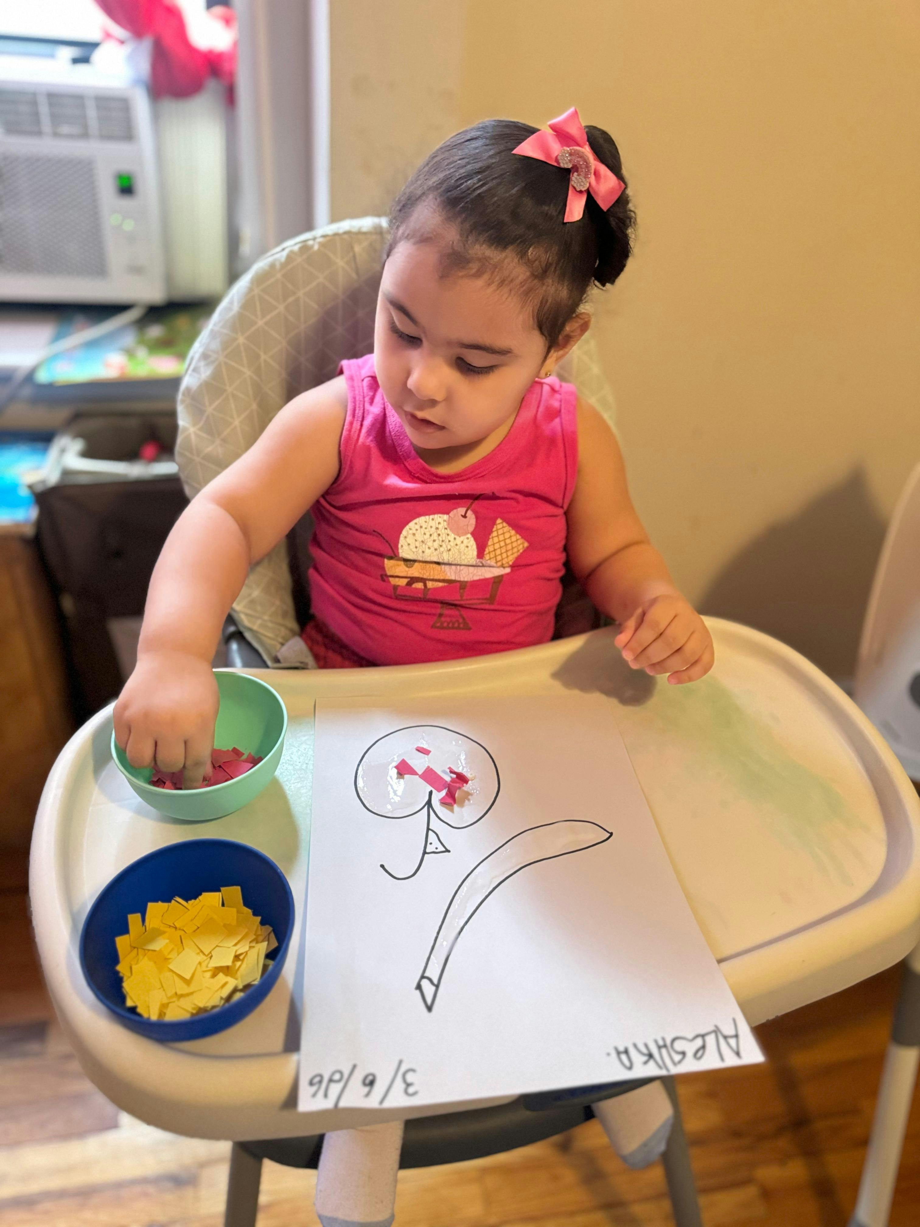 Child in high chair decorating paper flower with small paper squares