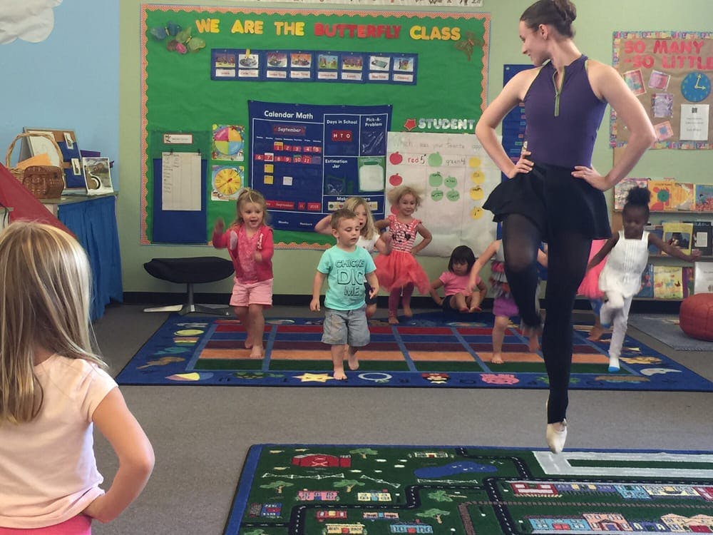 Adult and children in a classroom, adult demonstrating a ballet pose