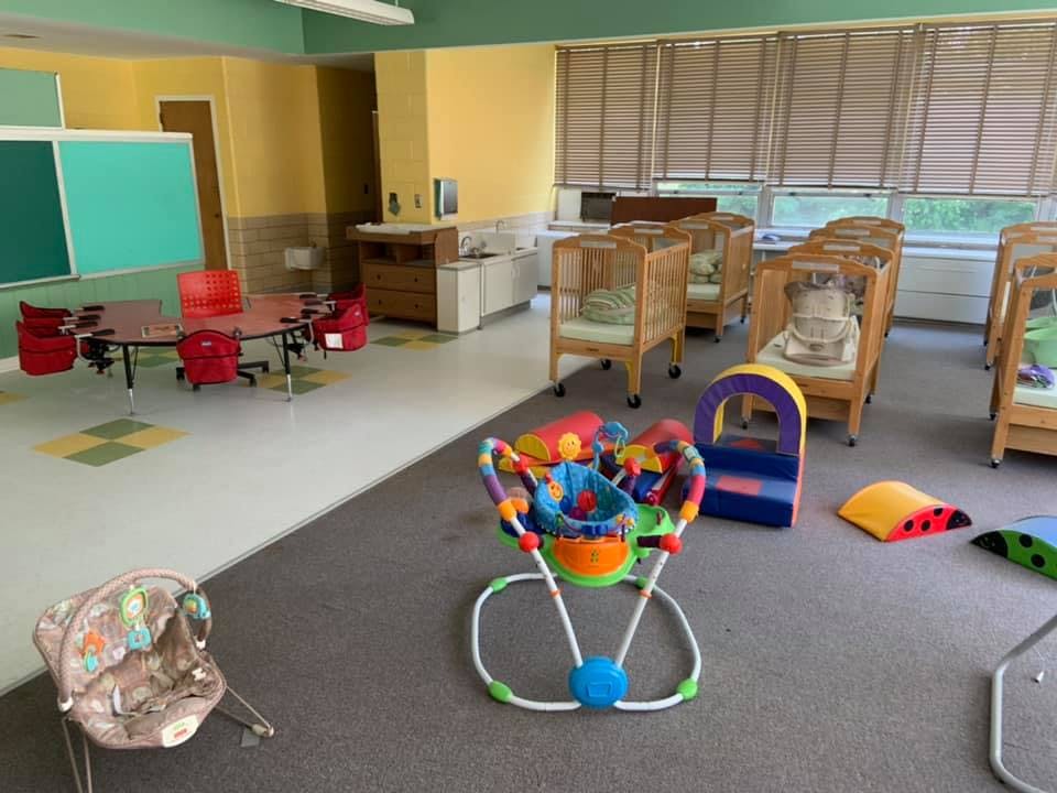 Daycare room with cribs, small tables and chairs, and baby activity toys