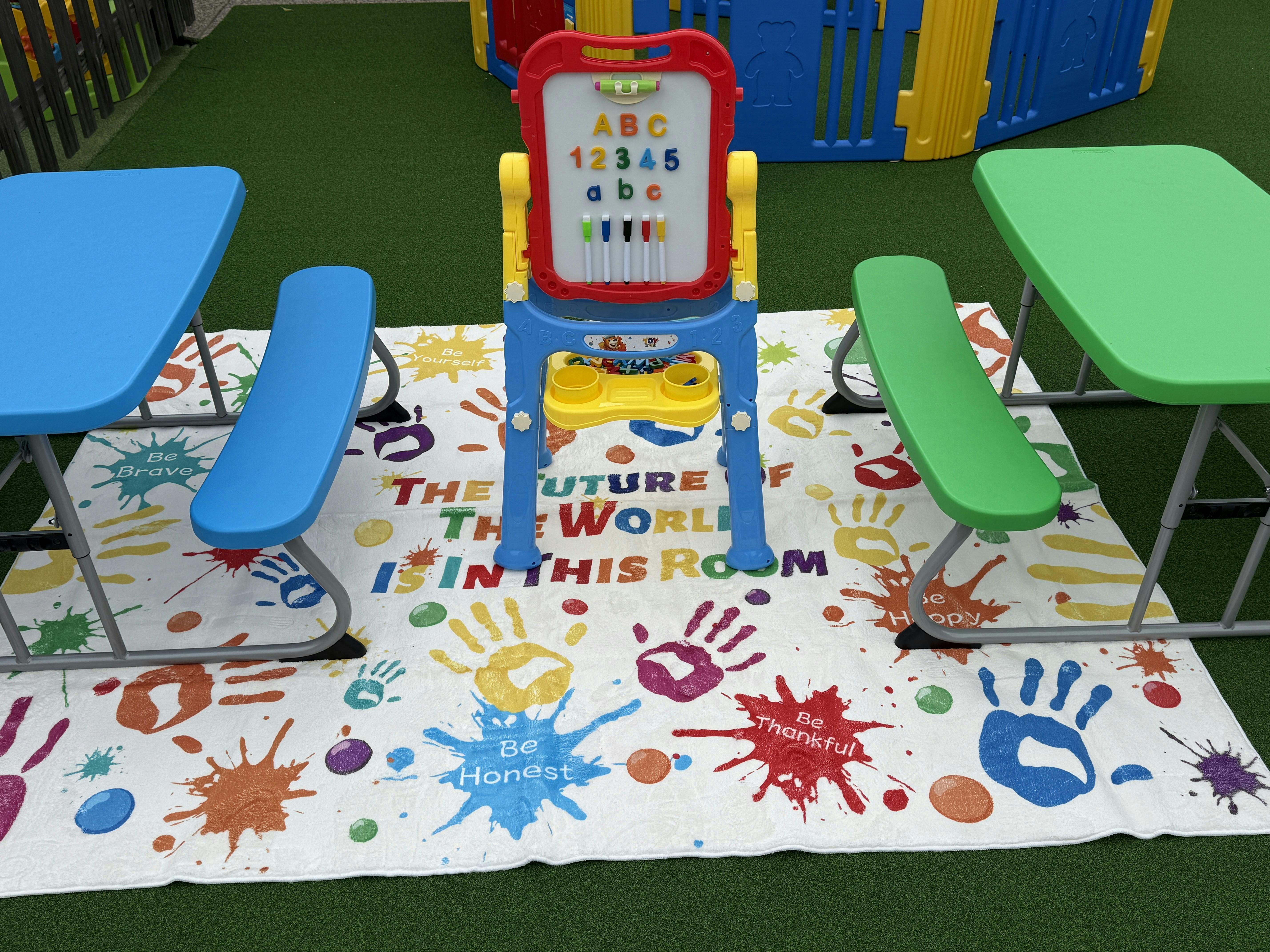 Children's play area with tables, benches, and an easel on a mat