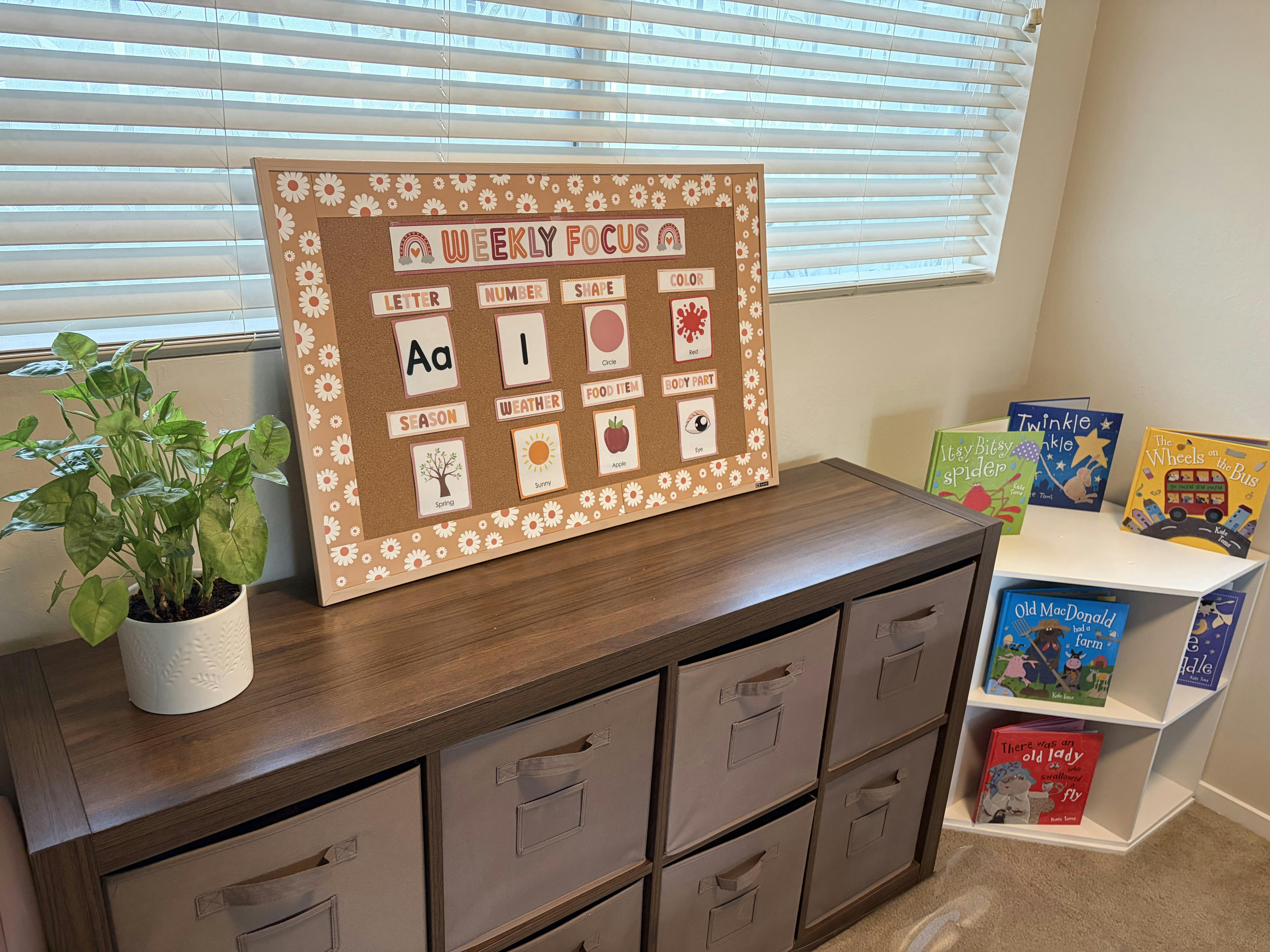 A classroom or childcare room with a \"Weekly Focus\" board and children's books