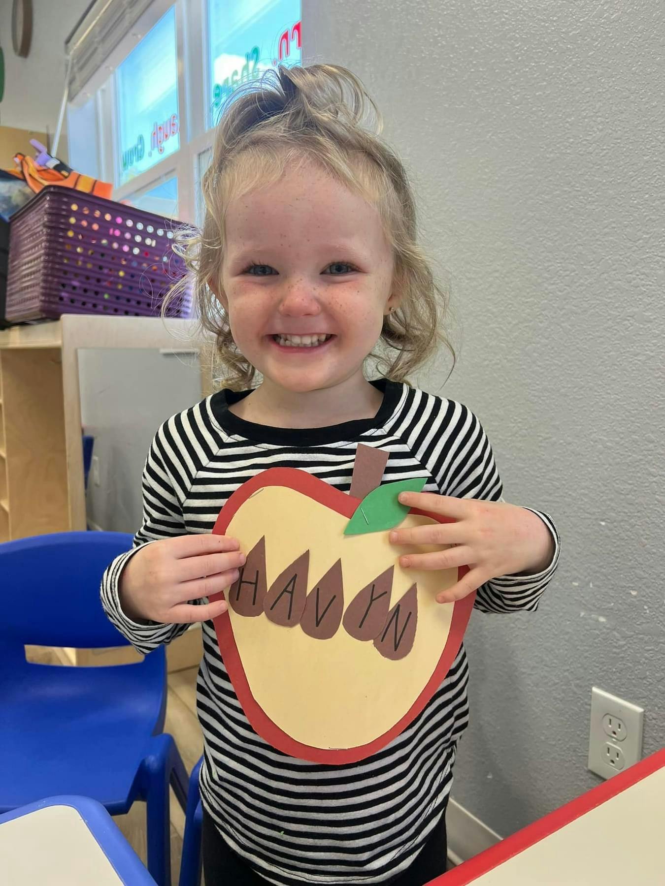 Child holding a paper apple with the name "HAVEN" on it