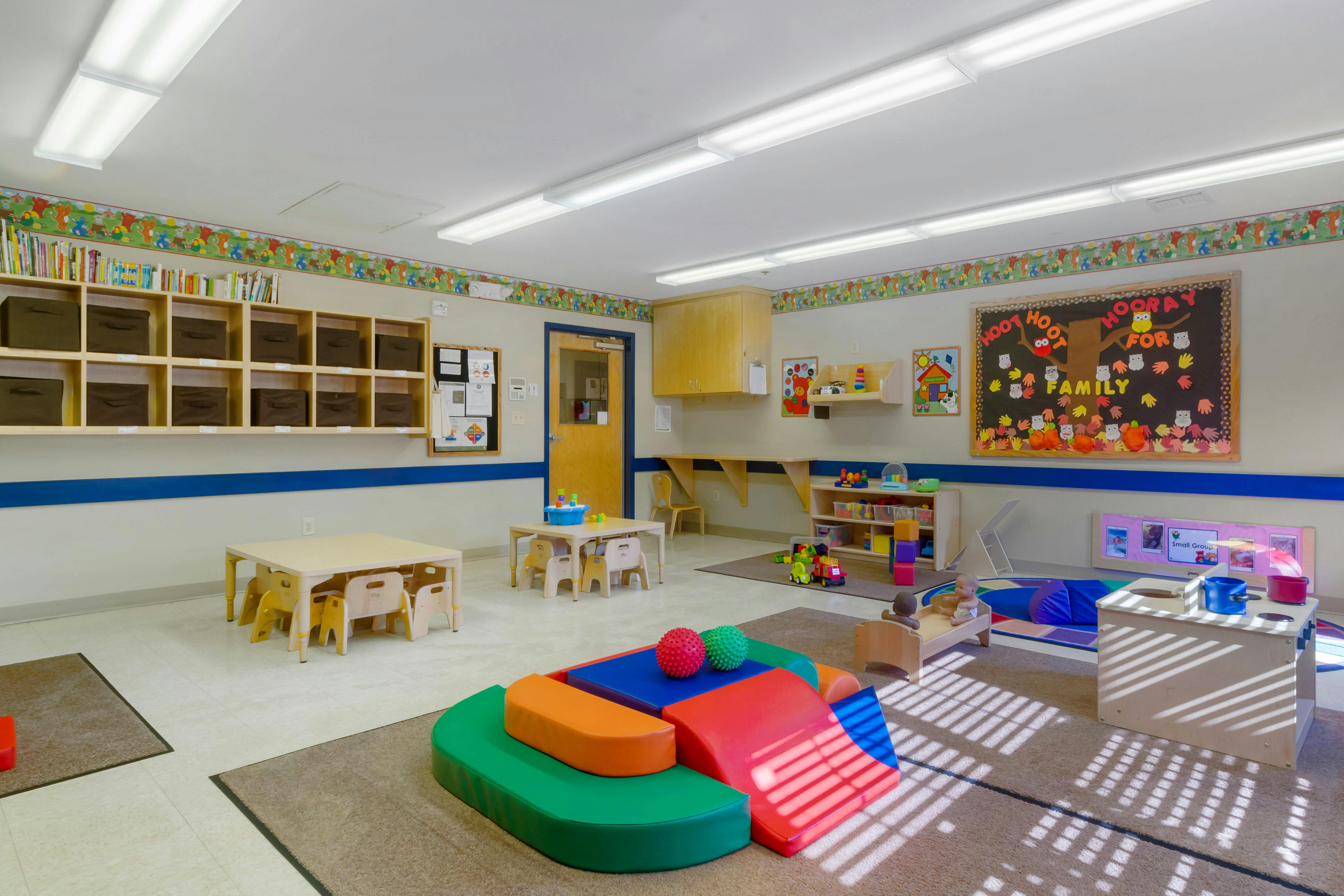 A colorful classroom with child-sized tables and chairs, play mats, and learning materials
