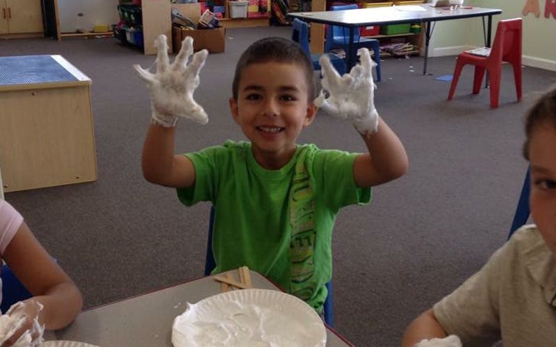 Child wearing gloves and holding hands up in a classroom