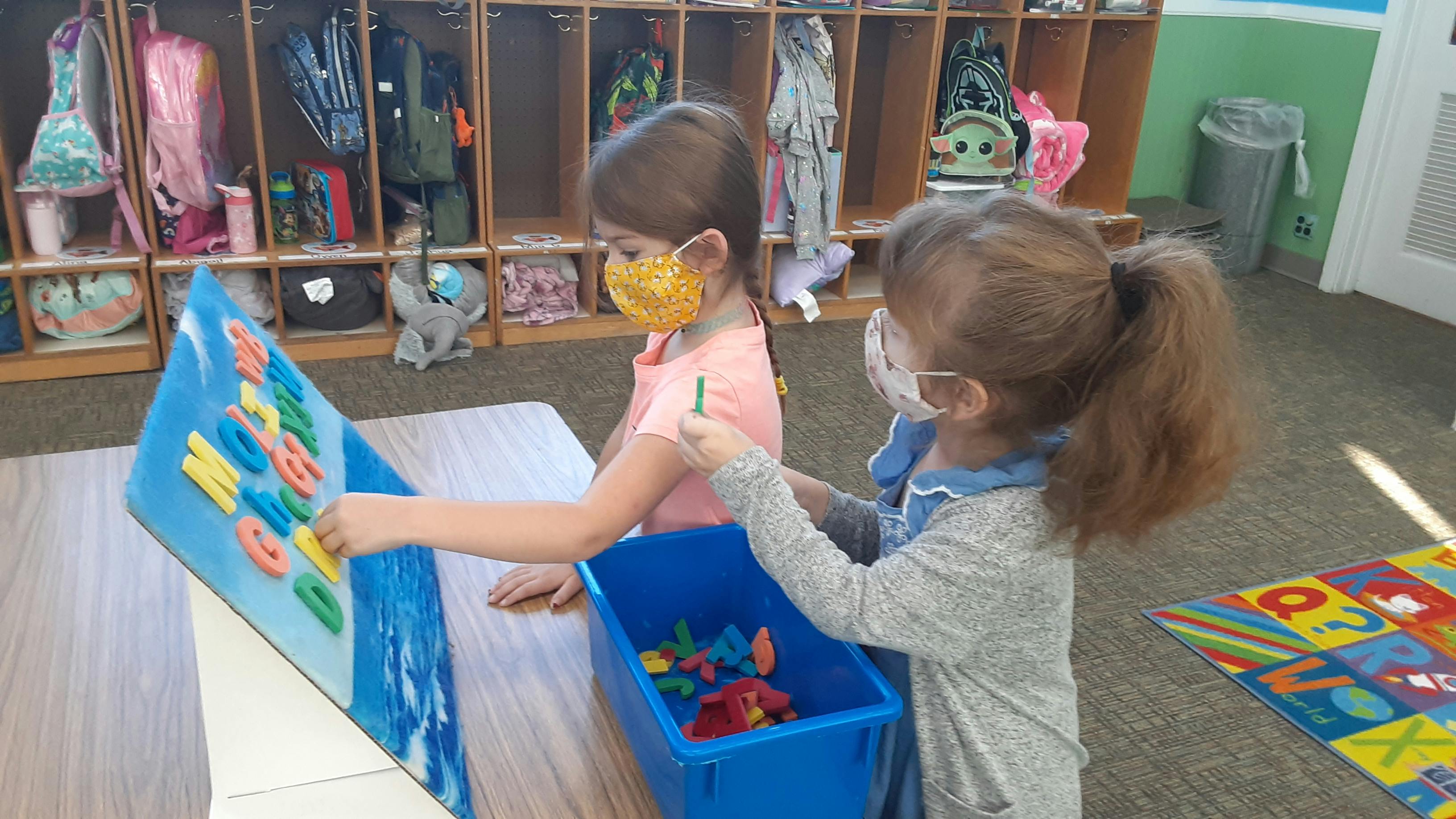 Two children in masks playing with colorful letters on a board
