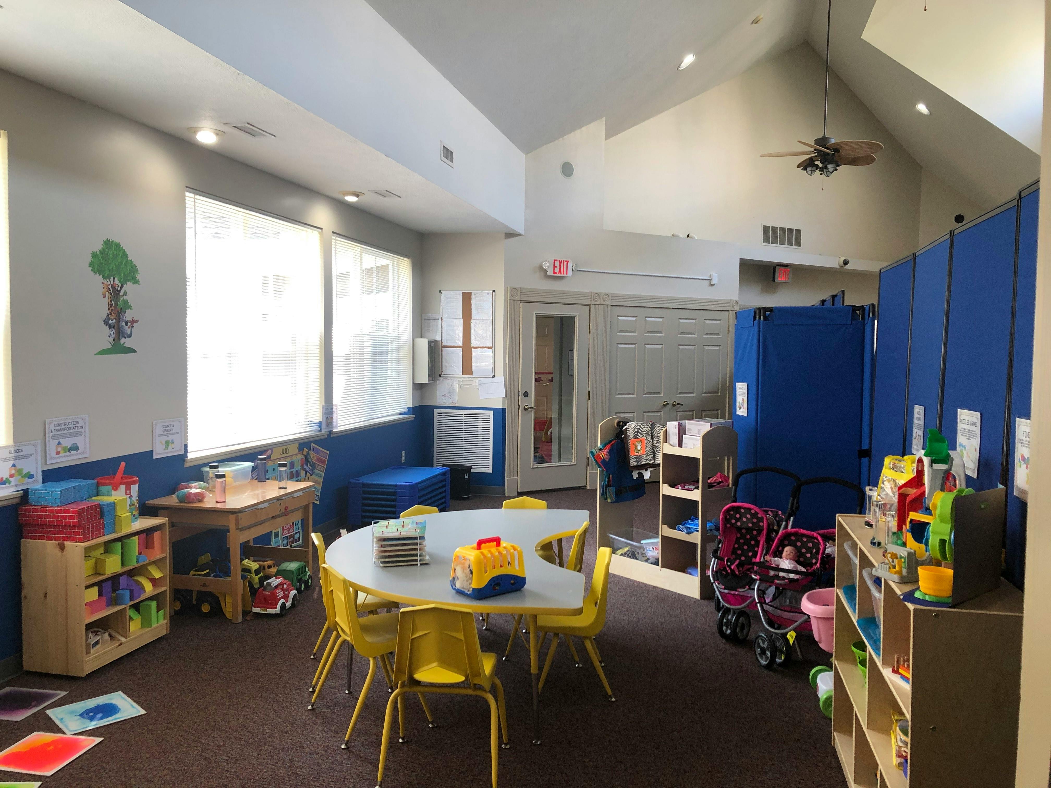 Playroom with small tables and chairs, toys, and blue partitions