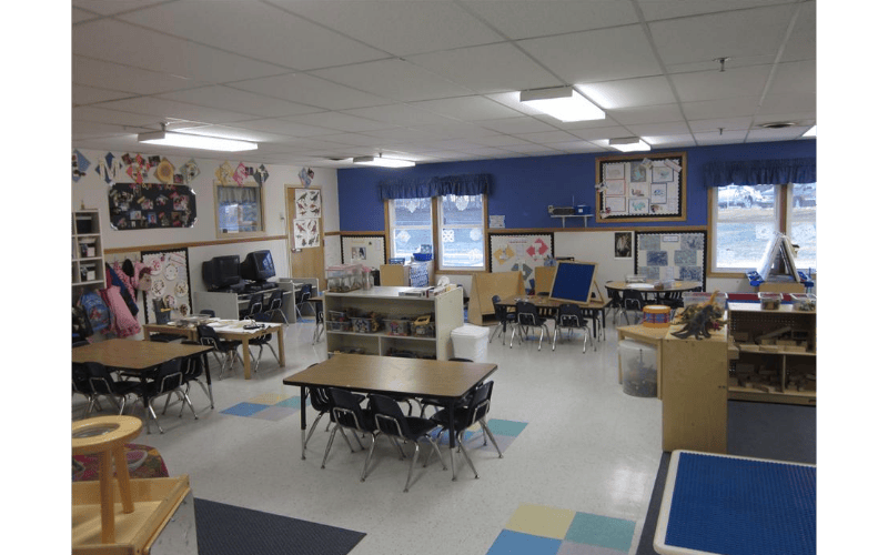 Empty classroom with small tables and chairs, artwork on walls