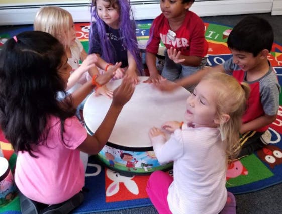 Children gathered around a large drum, playing it with their hands