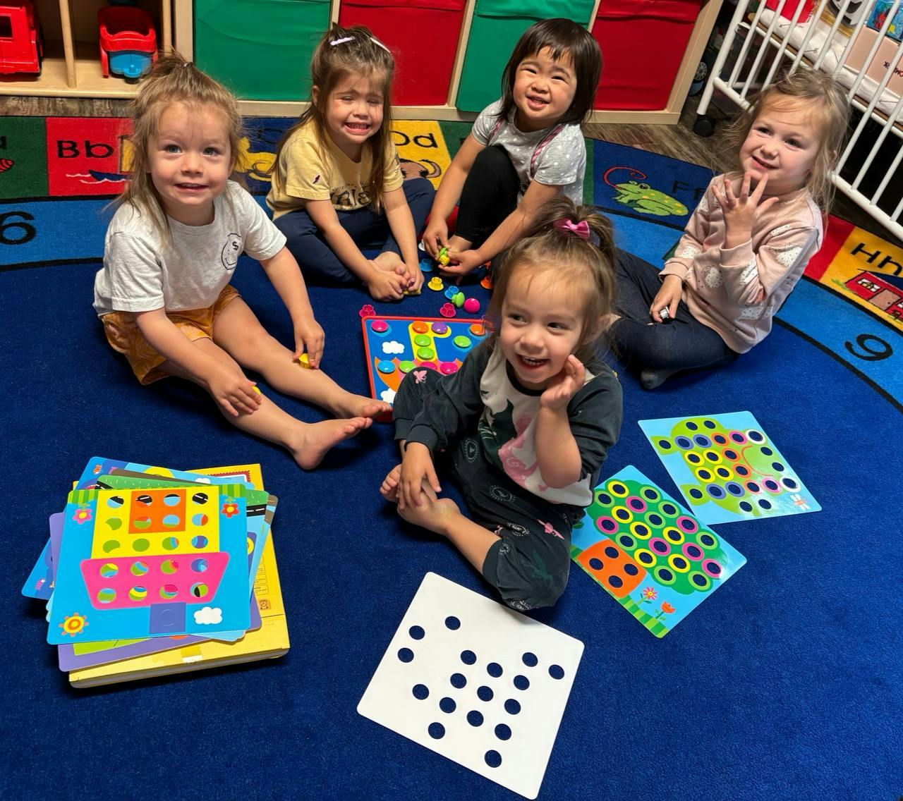 Five children sitting on a rug with colorful learning toys