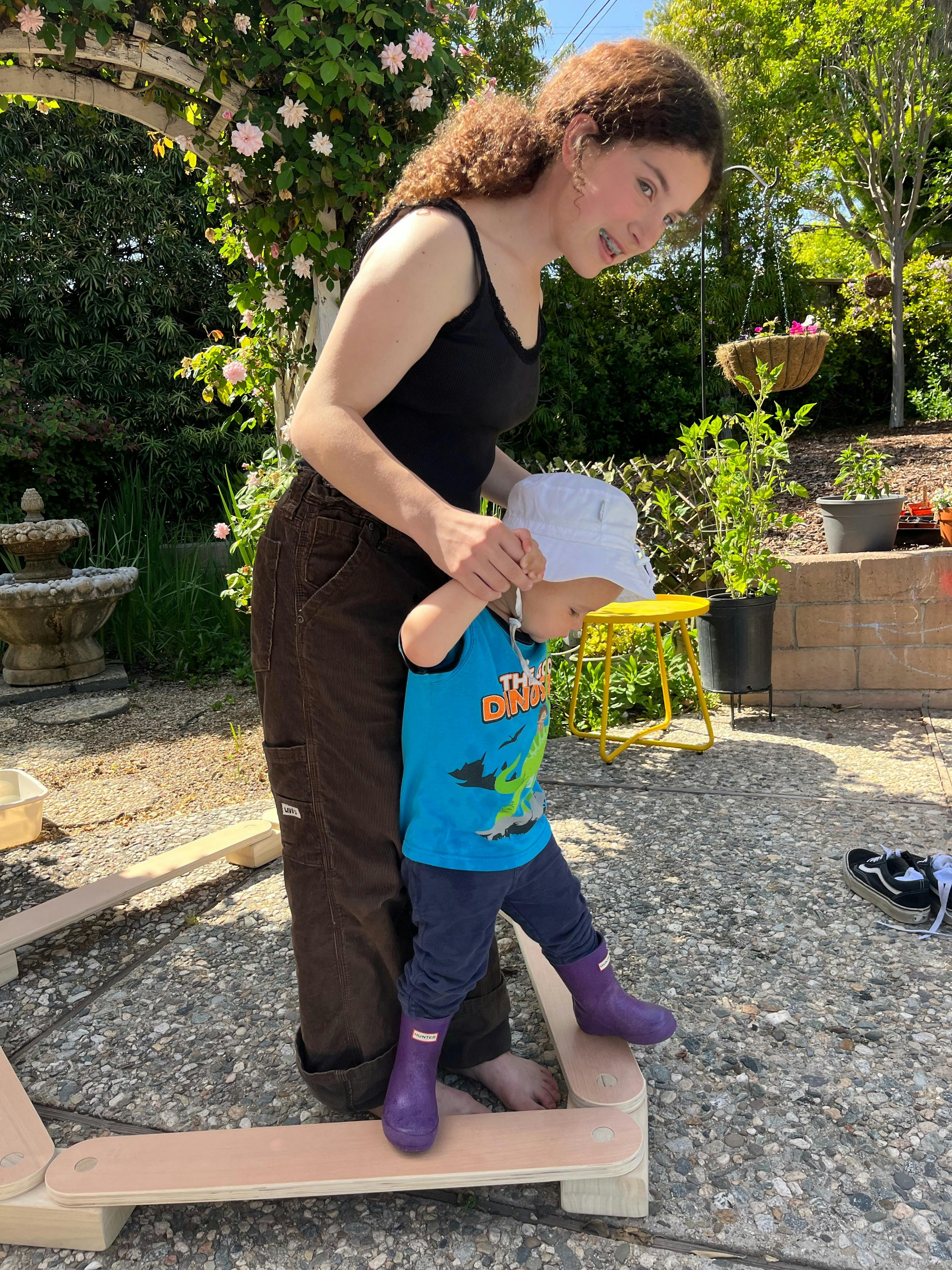Person helping a child walk on a wooden balance beam