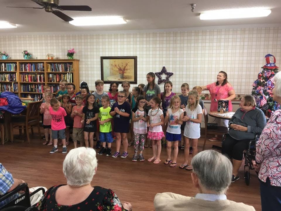 Group of children standing in a room with adults watching