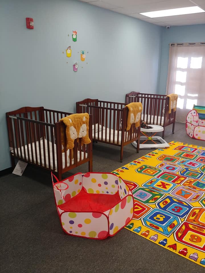Three cribs in a room with a colorful playmat and a soft playpen