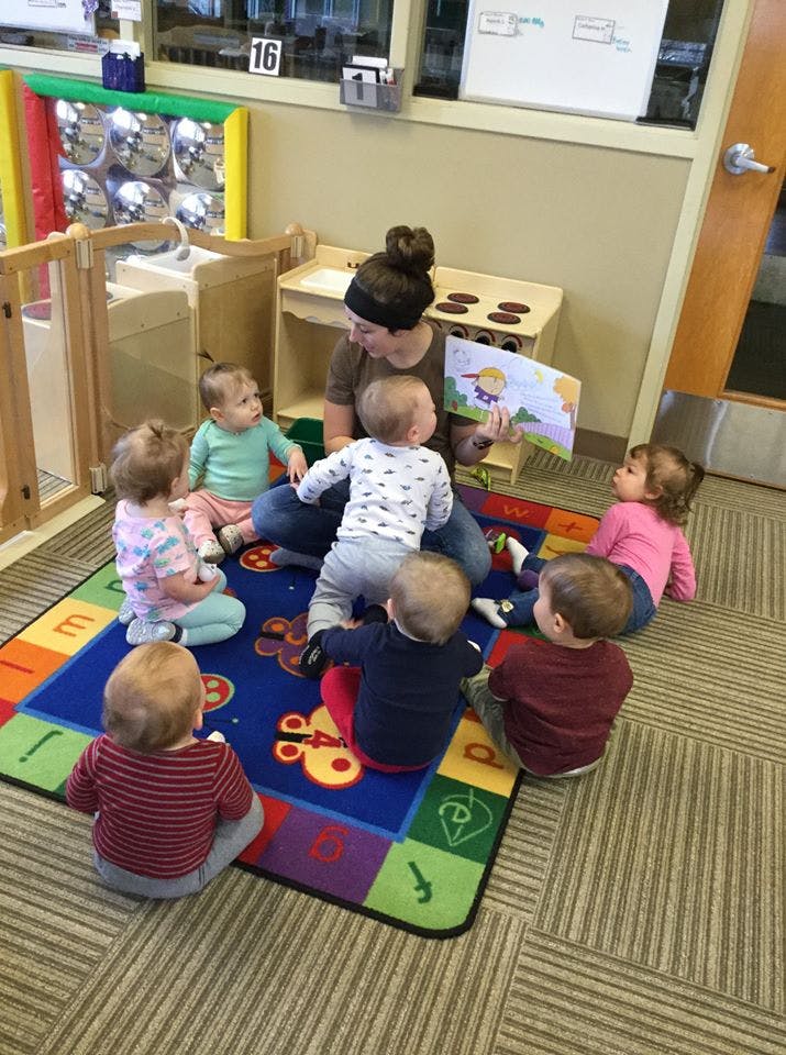 Adult reading a book to a group of children sitting on a colorful rug