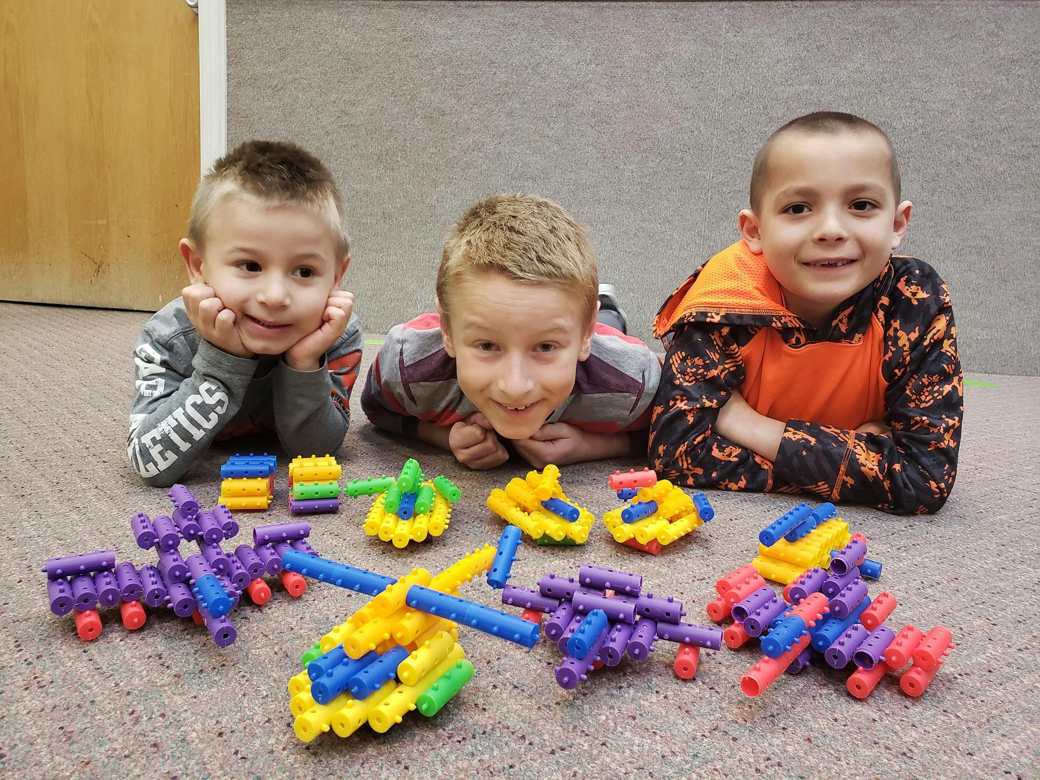 Three children lying on the floor with colorful block creations