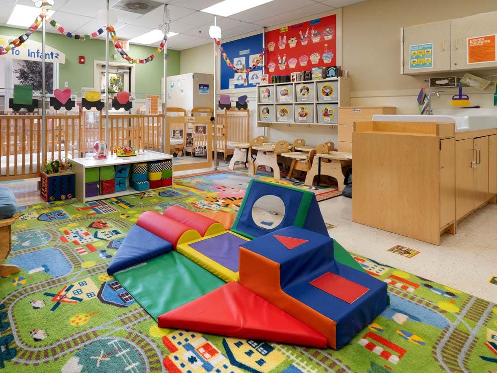 Colorful playroom with cribs, play mats, changing station, and cubbies