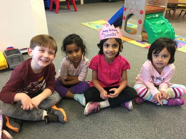 Four children sitting on the floor, one wearing a "Happy Birthday" crown