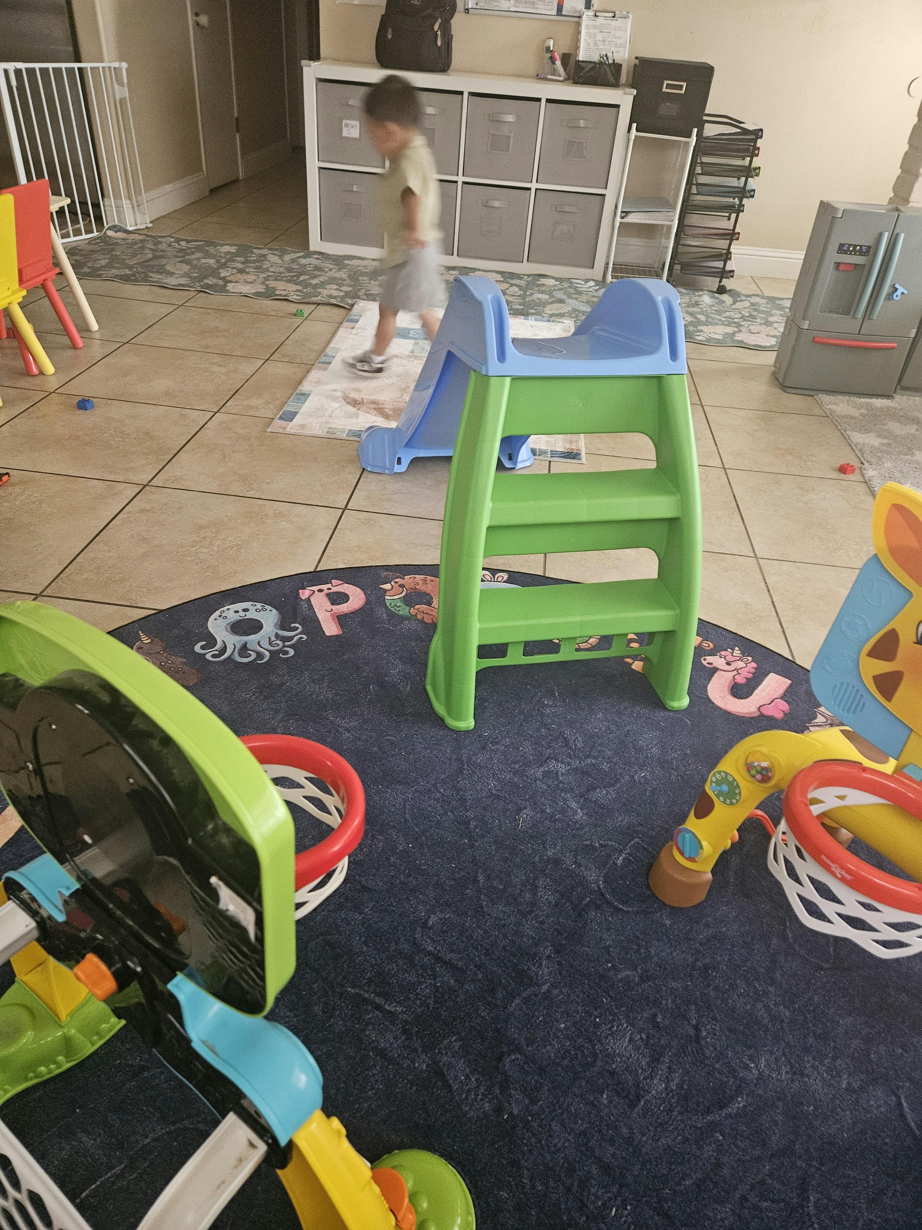 Child next to a blue and green plastic slide indoors