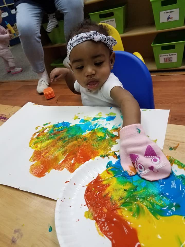 Child finger painting with a pink mitten on a table