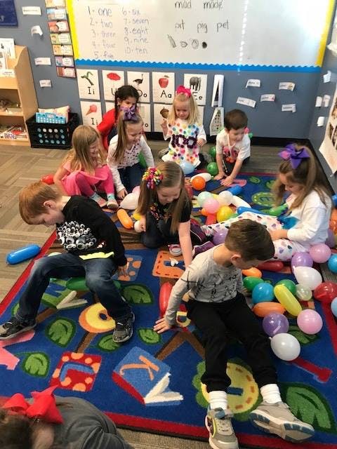 Children playing with balloons on a colorful rug in a classroom