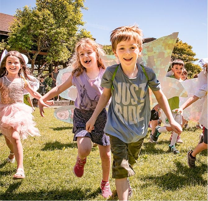 Group of children running across grass, some wearing wings
