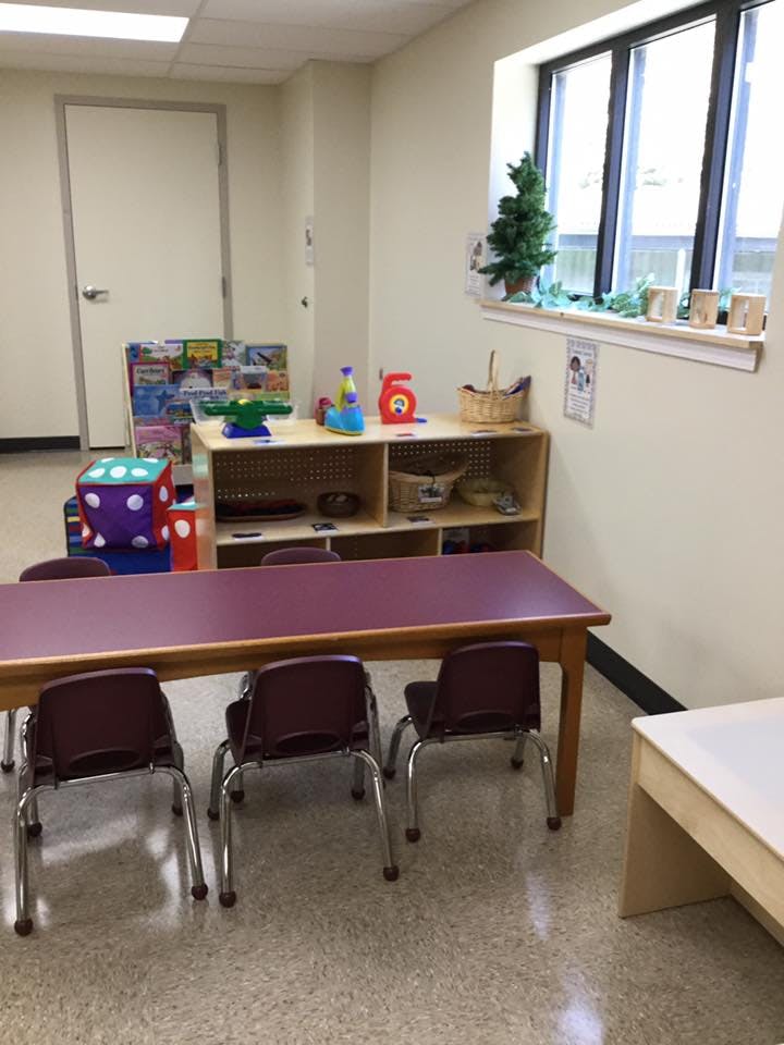 Classroom with small tables and chairs, shelves with toys, and a window