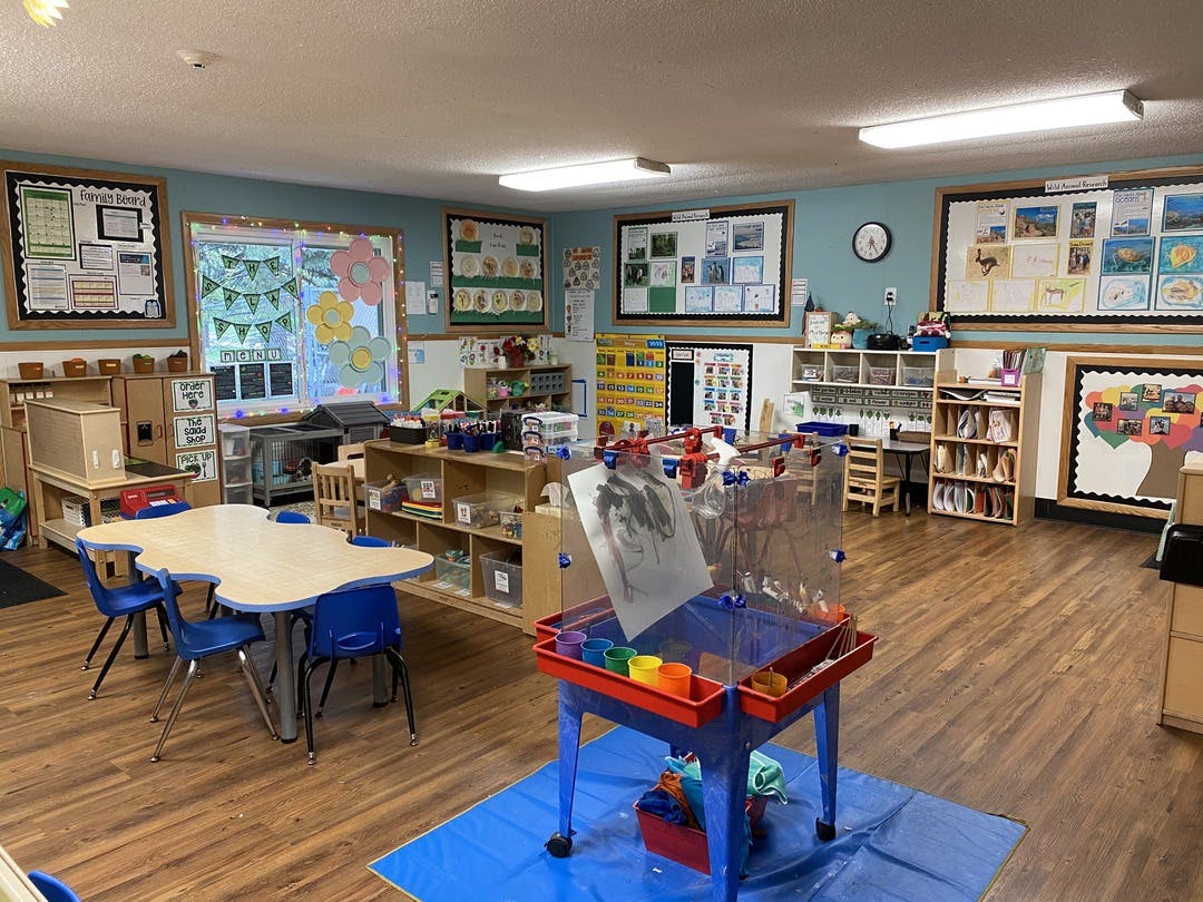 A classroom with a wooden floor, blue walls, and child-sized furniture