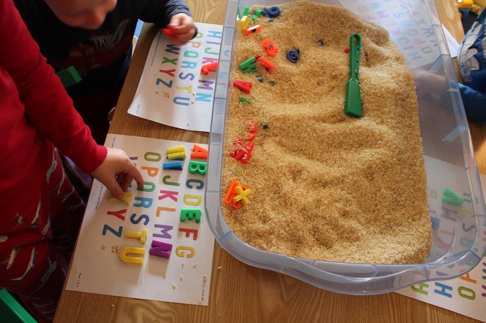 Child playing with alphabet letters and a sensory bin filled with rice