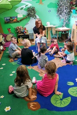 Adult and children sitting on a colorful rug in a classroom
