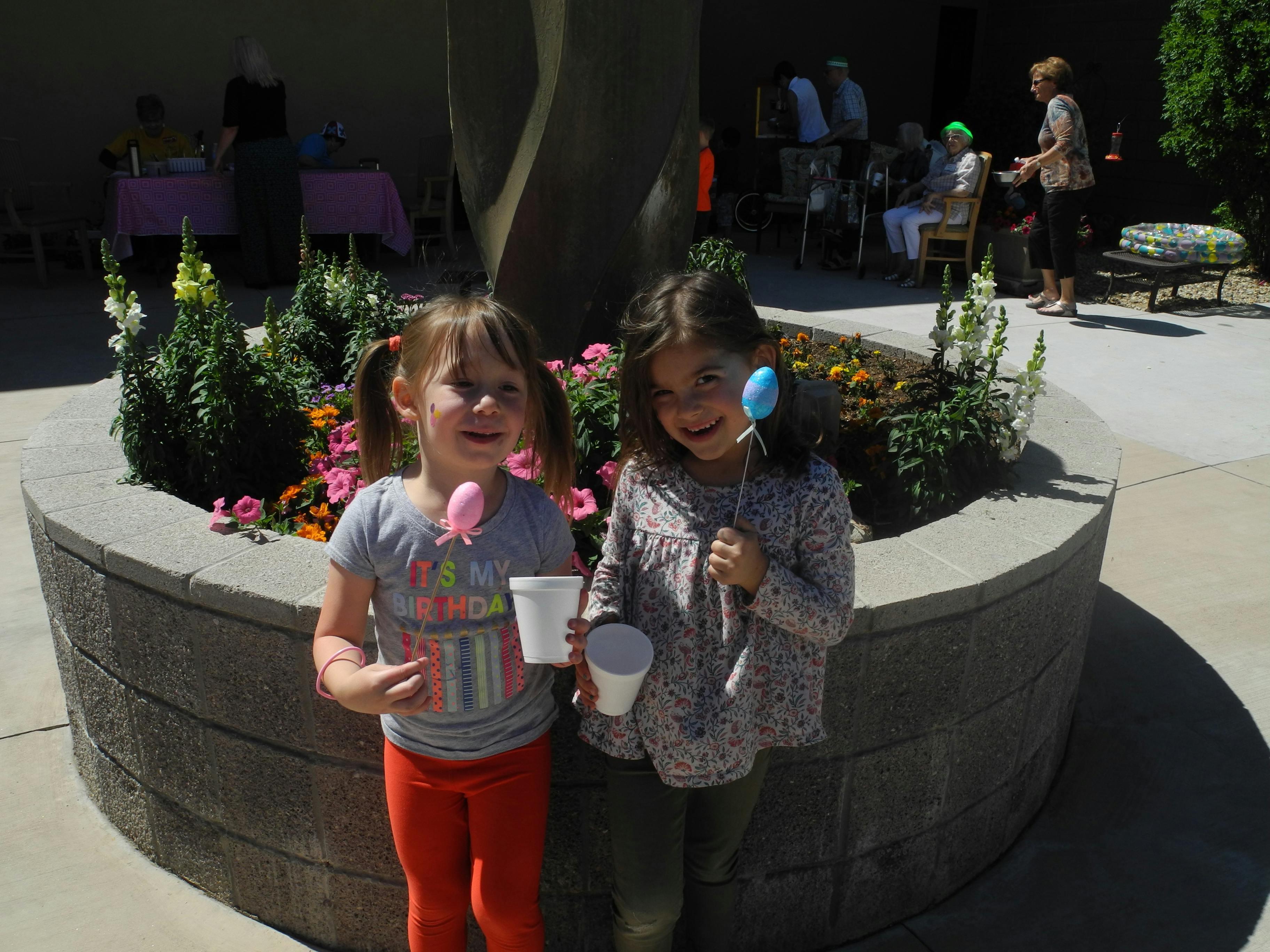 Two children holding cups and decorative eggs on sticks