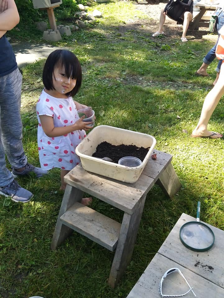 Child holding a cup next to a container of soil on a wooden stool