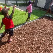Child playing on wood chips with another child in background