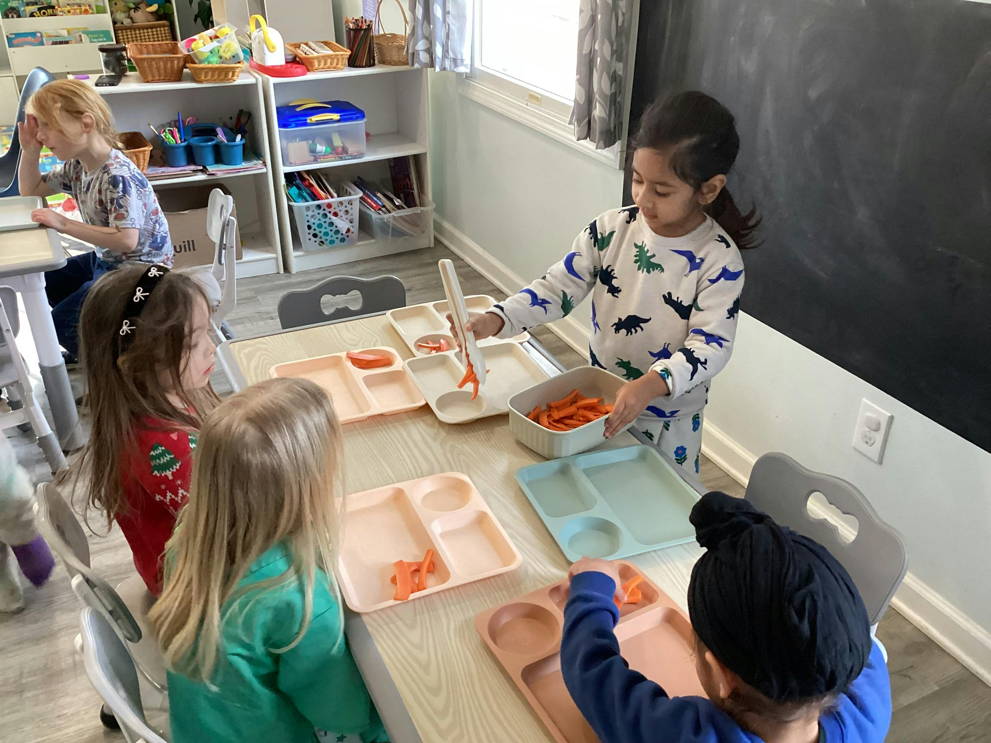 Child serving carrots onto a tray for other children at a table