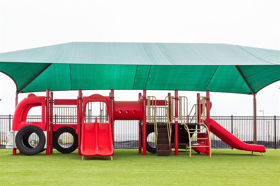 Red playground structure with slides and climbing areas under a green shade