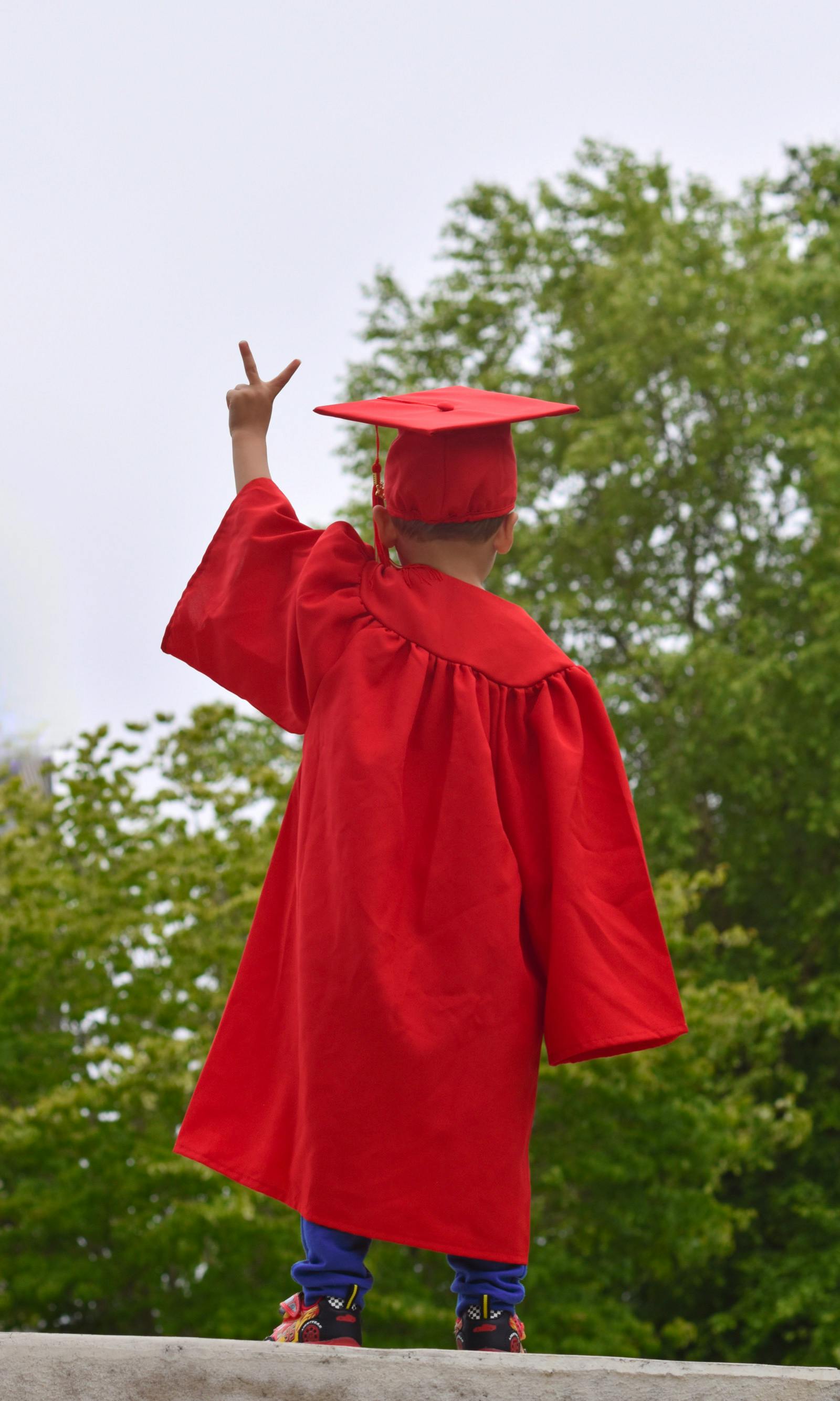 Child in red graduation cap and gown making a peace sign
