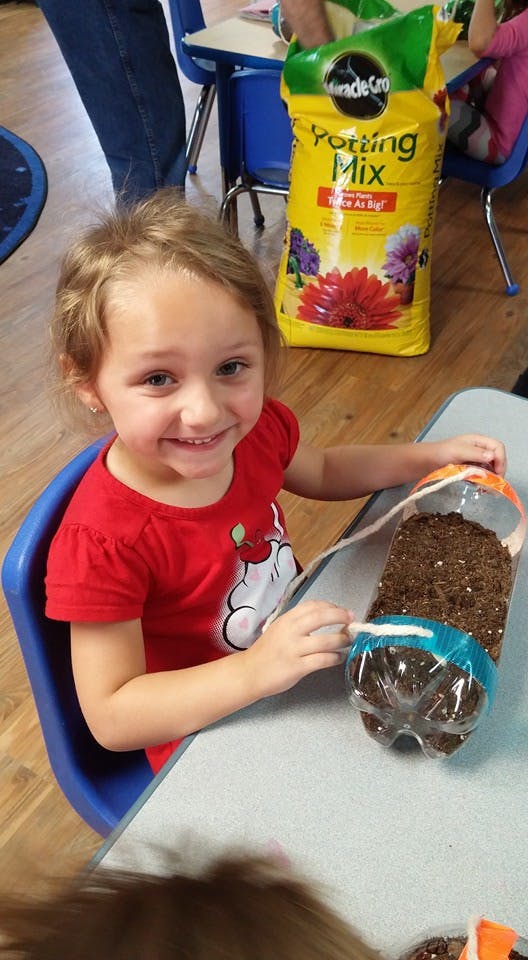 Child at a table with a plastic bottle filled with soil