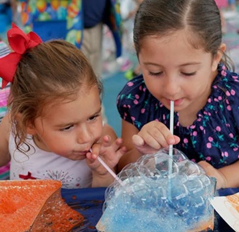 Two children blowing bubbles with straws into a blue liquid