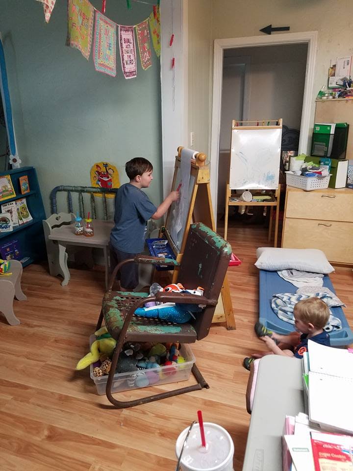Child drawing on an easel while another child sits on a mat