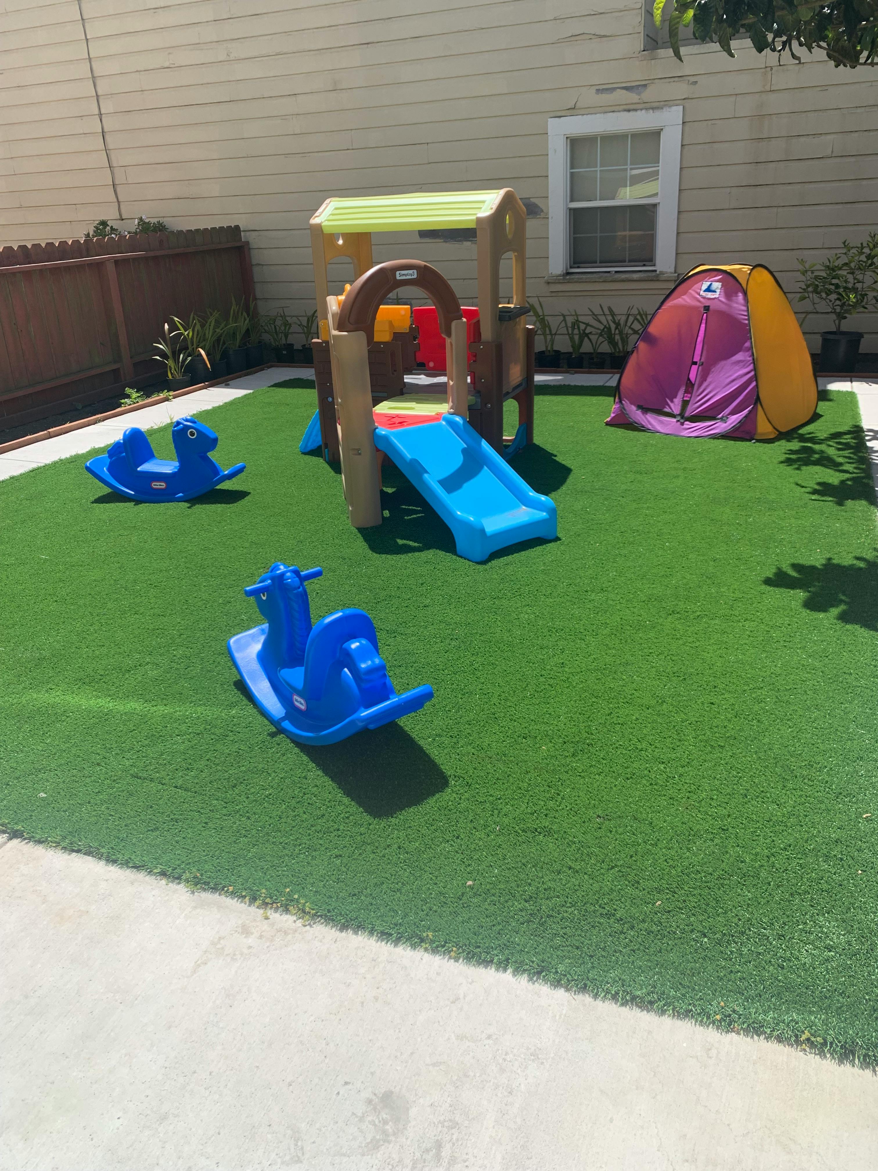 Playground with slide, two blue rocking toys, and a small tent on artificial grass