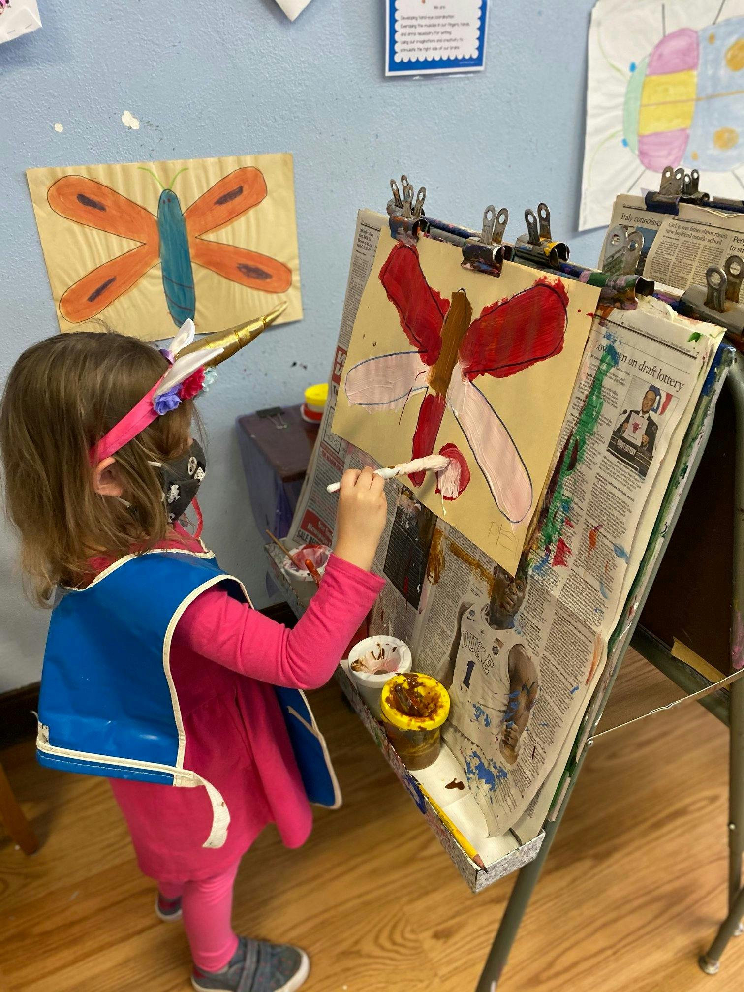 Child painting a butterfly on an easel in a classroom